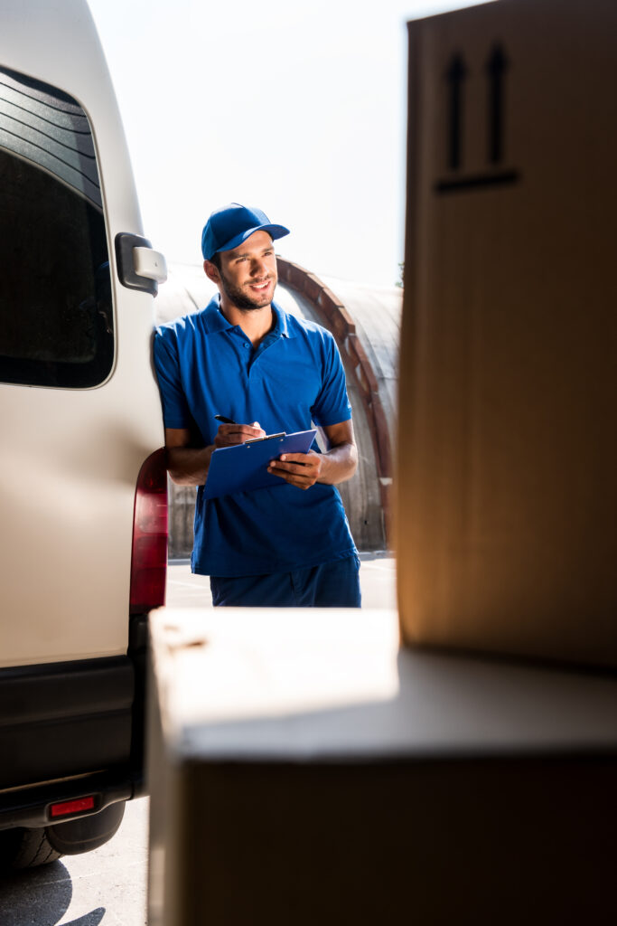 Transport Mitarbeiter neben einem Transporter notiert Anzahl von Kartons auf einer Checkliste