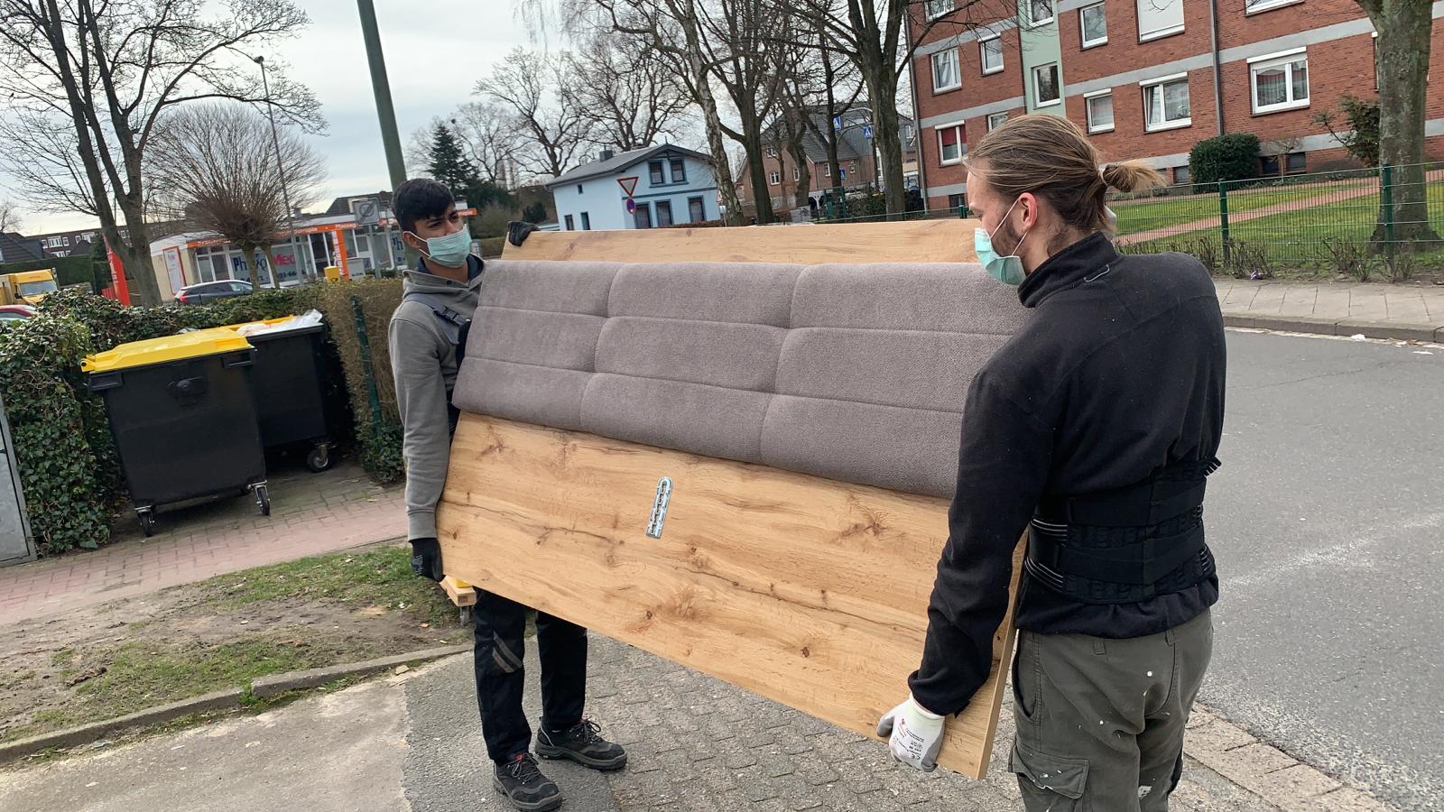 Zwei Umzugshelfer tragen schweres Möbelstück auf Strasse