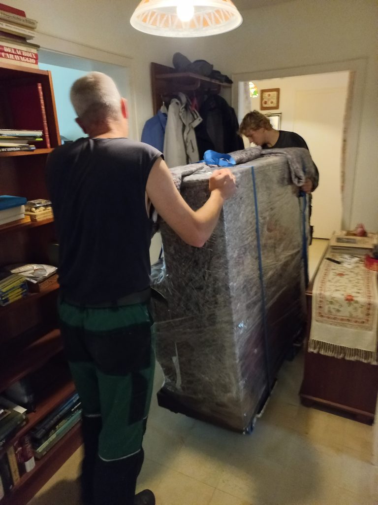 Mitarbeiter von Martens Transport transportieren ein verpacktes Klavier aus einer Wohnung ab